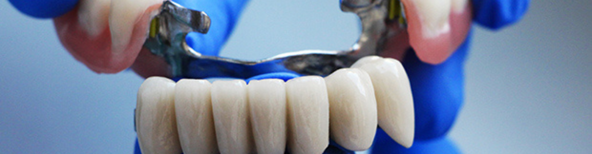 Gloved hands holding dental bridge and row of artificial teeth.